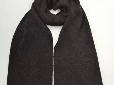Schwarzer Wollschal in grober Strickoptik, zu einer Schlaufe gelegt mit sichtbaren Rippstrick-Abschlüssen, Draufsicht auf weißem Hintergrund