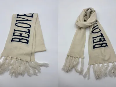 Heller Strickschal mit eingestricktem dunkelblauen Schriftzug und langen Quastenenden, flach ausgelegt und als Halsschal drapiert