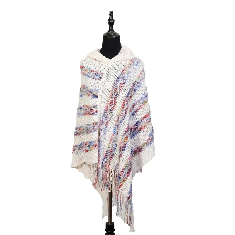 Elfenbeinfarbener Strickponcho mit Kapuze, buntem Streifenmuster in Rot und Blau sowie Fransenabschluss am Saum, auf schwarzer Schneiderpuppe präsentiert