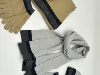Zwei dreiteilige Strick-Wintersets mit Mütze, Schal und Fäustlingen in Sandbeige und Hellgrau mit dunkleren Streifen, nebeneinander arrangiert