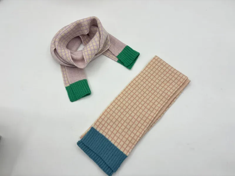 Zwei karierte Strickschals auf weißem Untergrund: lavendelfarbener Schal zur Schlaufe gelegt mit grünem Bündchen, beige-karierter Schal gefaltet mit blauem Rippabschluss