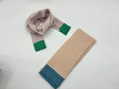 Zwei karierte Strickschals auf weißem Untergrund: lavendelfarbener Schal zur Schlaufe gelegt mit grünem Bündchen, beige-karierter Schal gefaltet mit blauem Rippabschluss