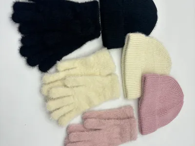 Drei aufeinander abgestimmte Sets aus flauschigen Strickhandschuhen und gerippten Wintermützen in Schwarz, Naturweiß und Altrosa auf weißem Hintergrund angeordnet