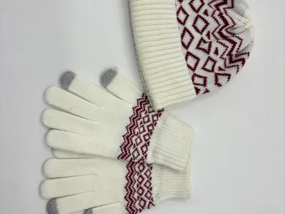 Cremeweiße Strickmütze und dazu passende Touchscreen-Handschuhe mit burgunderrotem geometrischem Fair-Isle-Muster, auf weißem Hintergrund