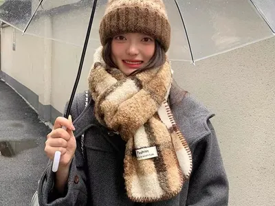 Damen-Winterset bestehend aus flauschigem Sherpa-Schal im Karomuster und grob gestrickter Pudelmütze in Braun-Creme unter Regenschirm