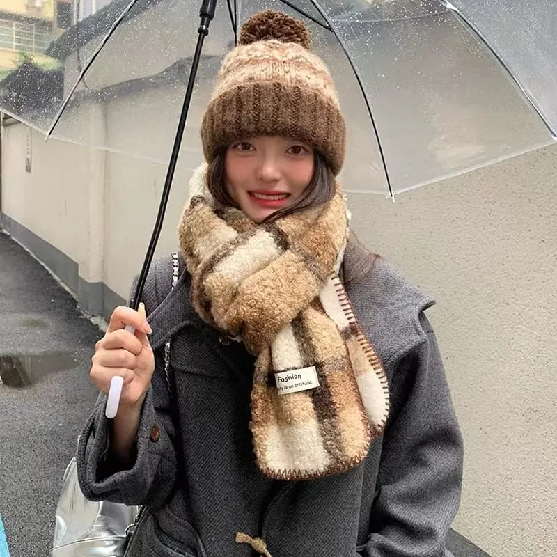Damen-Winterset bestehend aus flauschigem Sherpa-Schal im Karomuster und grob gestrickter Pudelmütze in Braun-Creme unter Regenschirm