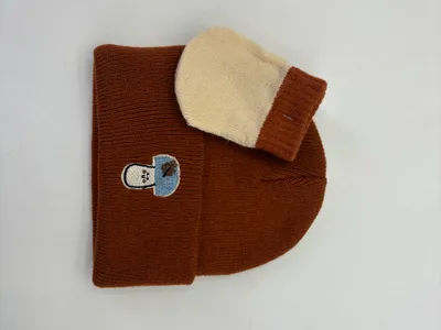 Braune Rippstrick-Wintermütze mit gesticktem Aufnäher, kombiniert mit cremefarbenem und braunem zweifarbigen Strickfäustling