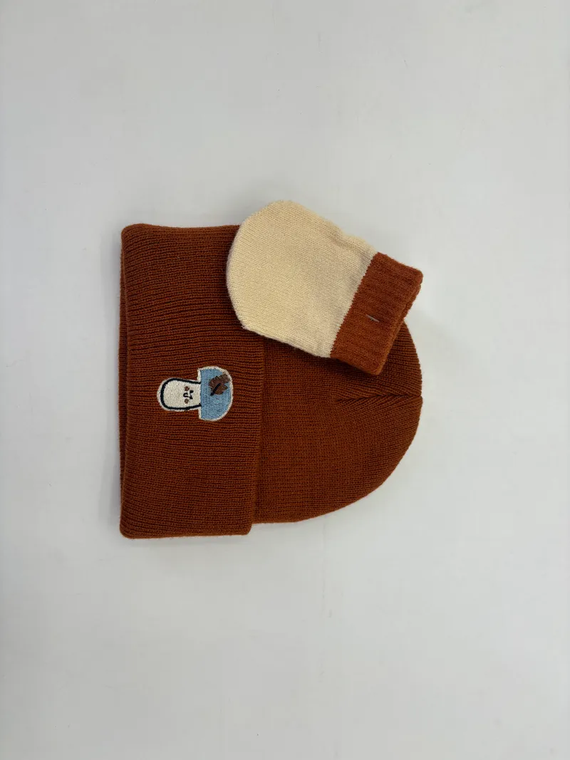 Braune Rippstrick-Wintermütze mit gesticktem Aufnäher, kombiniert mit cremefarbenem und braunem zweifarbigen Strickfäustling