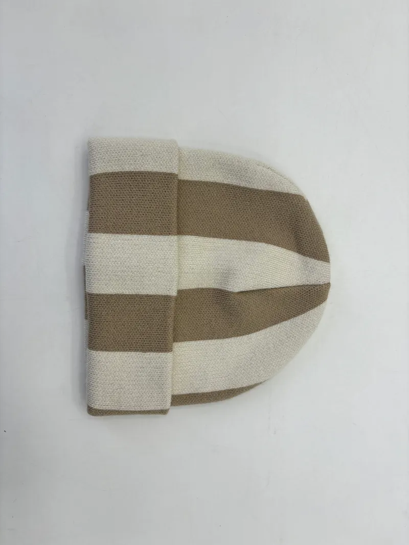 Flachliegende Strickmütze mit breiten senkrechten Streifen in Beige und Naturweiß mit Umschlagrand, auf weißem Untergrund