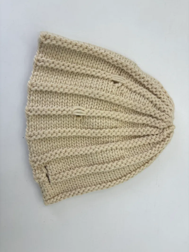 Draufsicht einer cremefarbenen, grob gerippten Strickmütze aus natürlichem Elfenbein-Garn, gefaltet zur Ansicht der Stricktextur