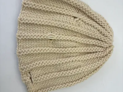 Draufsicht einer cremefarbenen, grob gerippten Strickmütze aus natürlichem Elfenbein-Garn, gefaltet zur Ansicht der Stricktextur