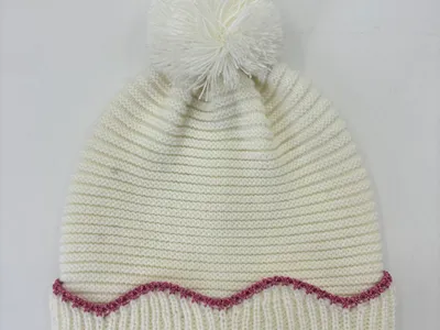 Cremefarben grob gestrickte Wintermütze mit fluffigem Bommel oben und dekorativer rosa Zickzack-Stickerei am Rand