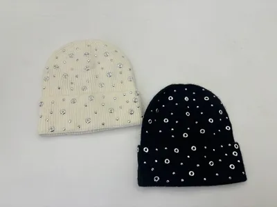 Zwei Rippstrickmützen in Creme und Schwarz mit silbernen Ösenringen und Strasssteinen dekoriert, auf weißem Hintergrund