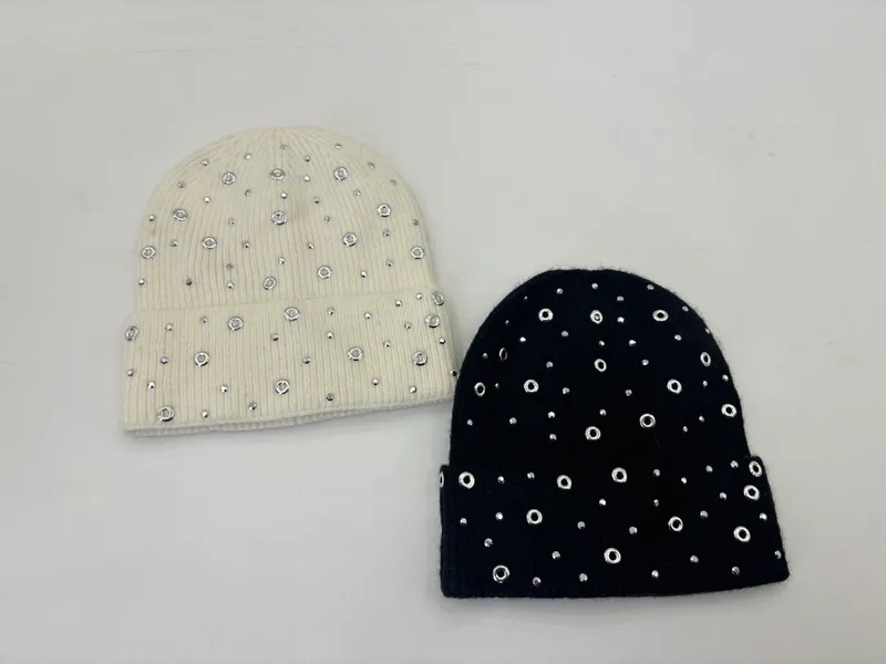 Zwei Rippstrickmützen in Creme und Schwarz mit silbernen Ösenringen und Strasssteinen dekoriert, auf weißem Hintergrund