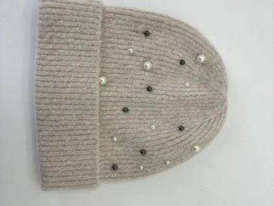 Flach liegend: Beige Rippstrickmütze mit vereinzelten weißen Perlen und dunklen Kristallnieten dekoriert, weißer Hintergrund