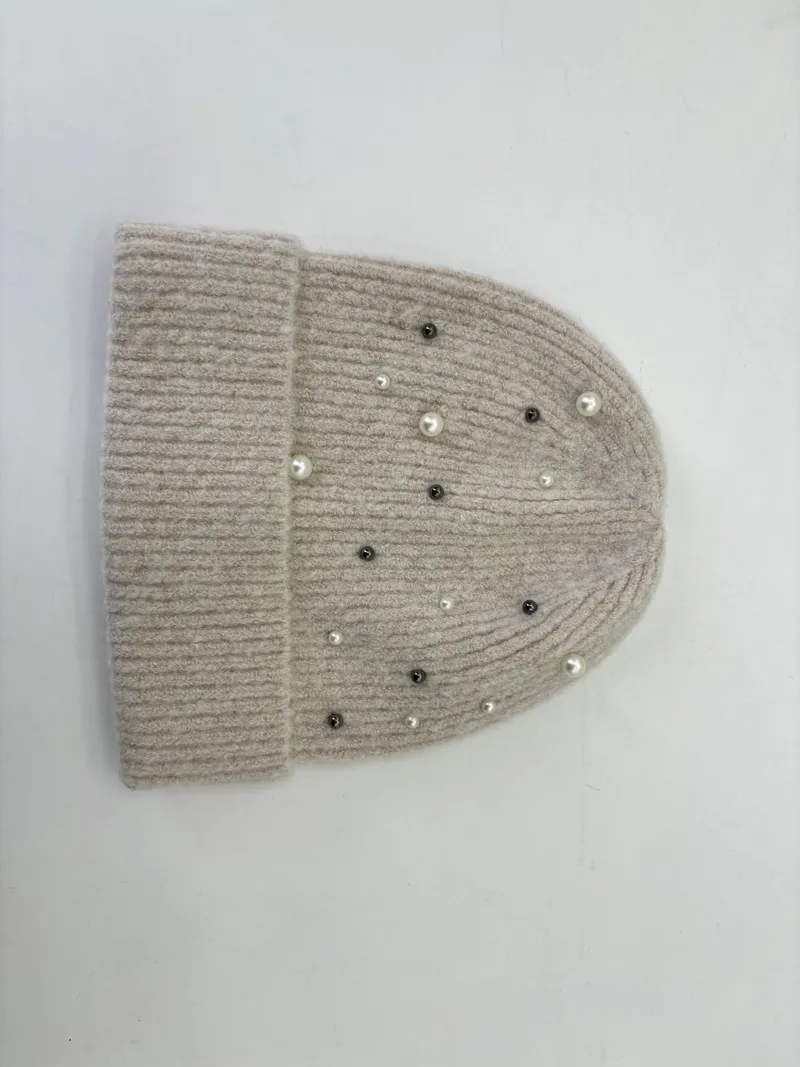 Flach liegend: Beige Rippstrickmütze mit vereinzelten weißen Perlen und dunklen Kristallnieten dekoriert, weißer Hintergrund