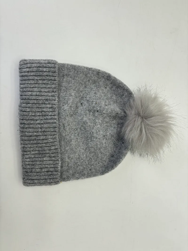 Hellgraue Wintermütze aus Strickstoff mit fluffigem Kunstfell-Pompom und funkelnden Kristallsteinen am Rippenbündchen