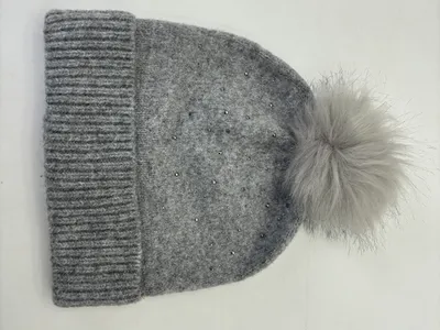 Hellgraue Wintermütze aus Strickstoff mit fluffigem Kunstfell-Pompom und funkelnden Kristallsteinen am Rippenbündchen