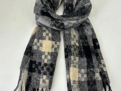 Gefalteter Webschal in Schwarz, Grau und Creme mit Patchwork-Karomuster und Quastfransen auf weißem Hintergrund