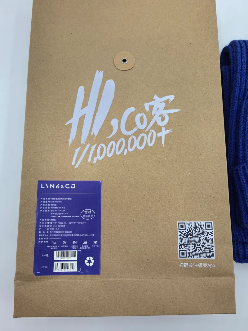 Marineblaues Grob-Strickset aus Wollschal und Beanie-Mütze in einer nachhaltigen Kraftpapier-Umschlagtasche mit Produktetikett