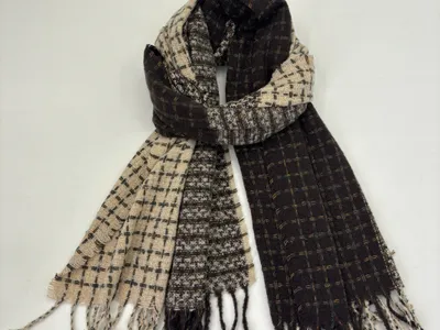 Zweifarbiger Schal im Schachbrettmuster aus Schwarz und Beige mit geknoteten Fransenenden, flach liegend