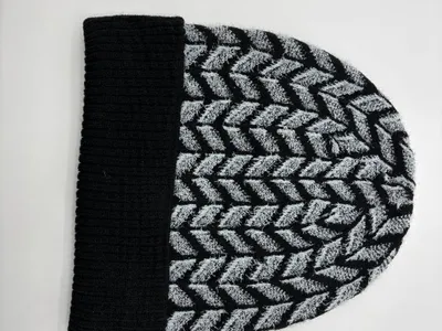 Strickmütze in Schwarz und Grau mit Chevron-Fischgrätmuster und schwarzem Rippenbündchen, flach auf weißem Untergrund