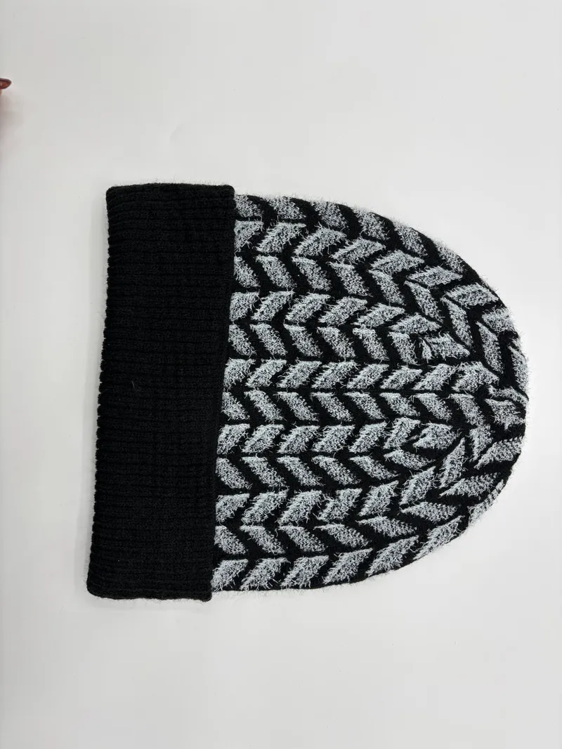 Strickmütze in Schwarz und Grau mit Chevron-Fischgrätmuster und schwarzem Rippenbündchen, flach auf weißem Untergrund