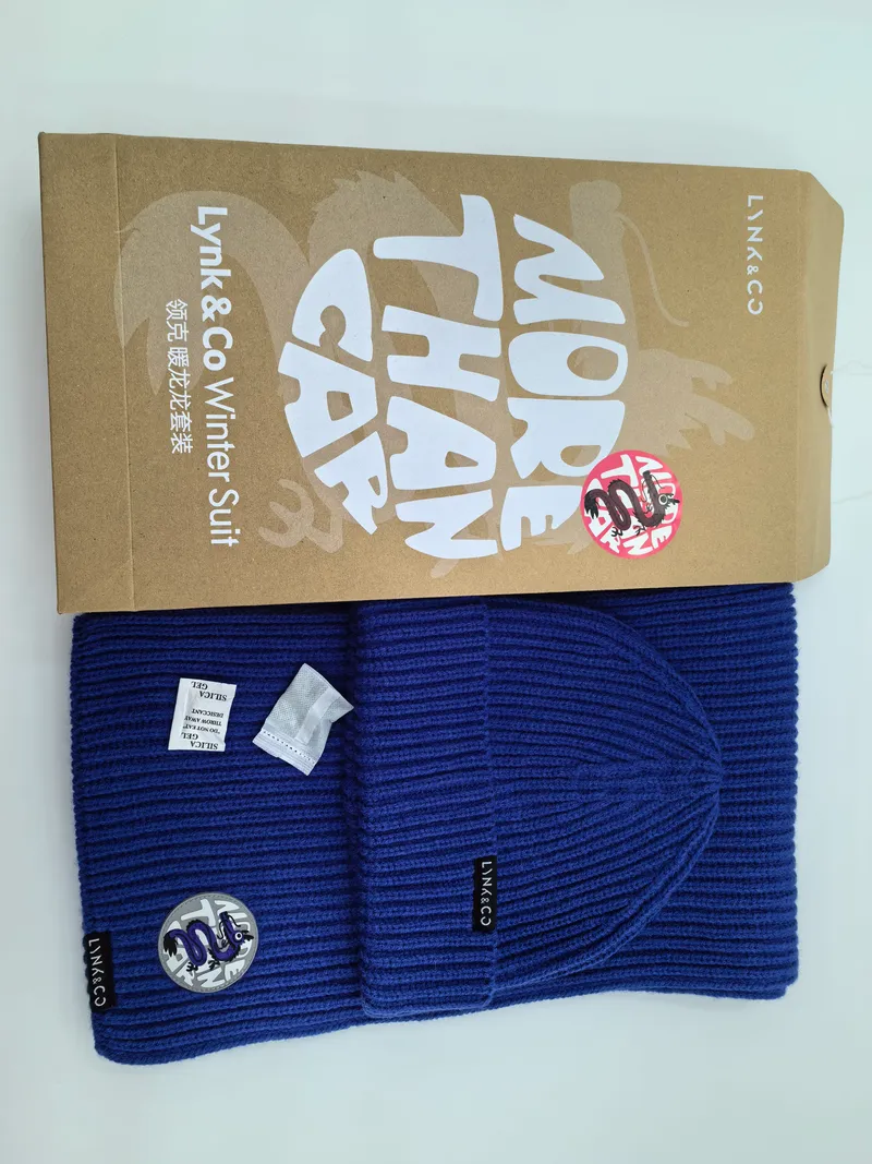 Royalblaue Rippenstrick-Wintermütze und passender Schal als flache Draufsicht, daneben eine Kraftpapier-Geschenkbox