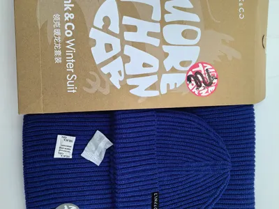 Royalblaue Rippenstrick-Wintermütze und passender Schal als flache Draufsicht, daneben eine Kraftpapier-Geschenkbox