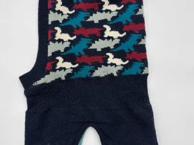 Ärmelloser Hundepullover in Dunkelblau mit farbenfrohem abstraktem Vogel-Intarsia-Muster in Petrol, Bordeaux und Creme, flach fotografiert