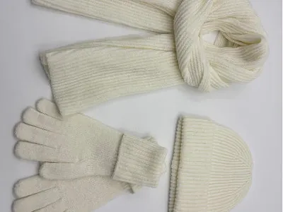 Dreiteiliges Winteraccessoire-Set in Cremeweiß mit langem Rippenstrickschal, Umschlagmütze und Fingerhandschuhen auf weißem Hintergrund