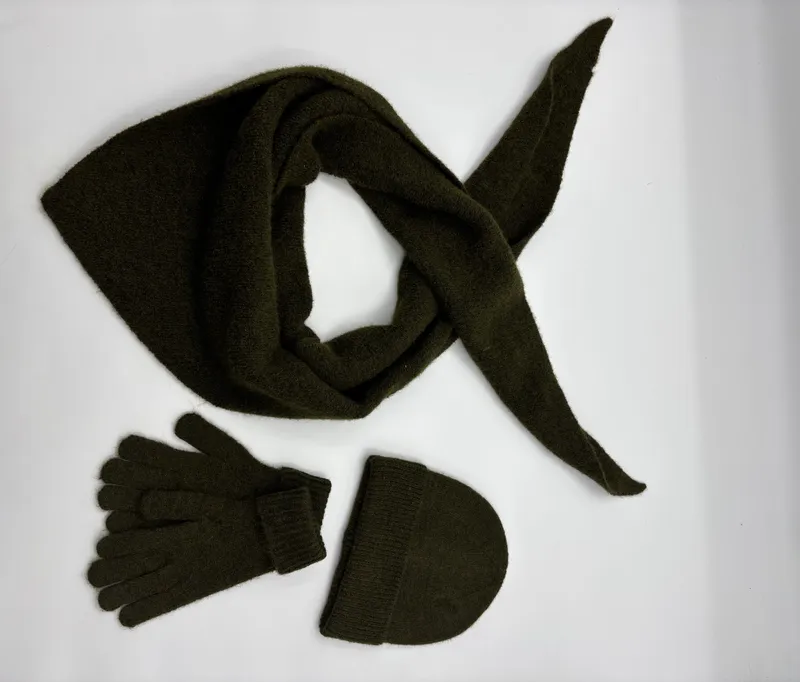 Olivgrünes Winteraccessoire-Set mit dreieckigem Stricktuch, anliegenden Handschuhen und Rippenstrickmütze auf weißem Hintergrund