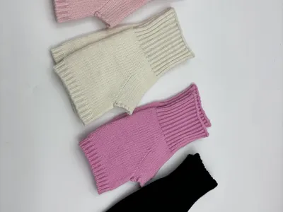 Vier fingerfreie Rippenstrickhandschuhe in Rosa, Creme, Flieder und Schwarz nebeneinander auf hellem Untergrund