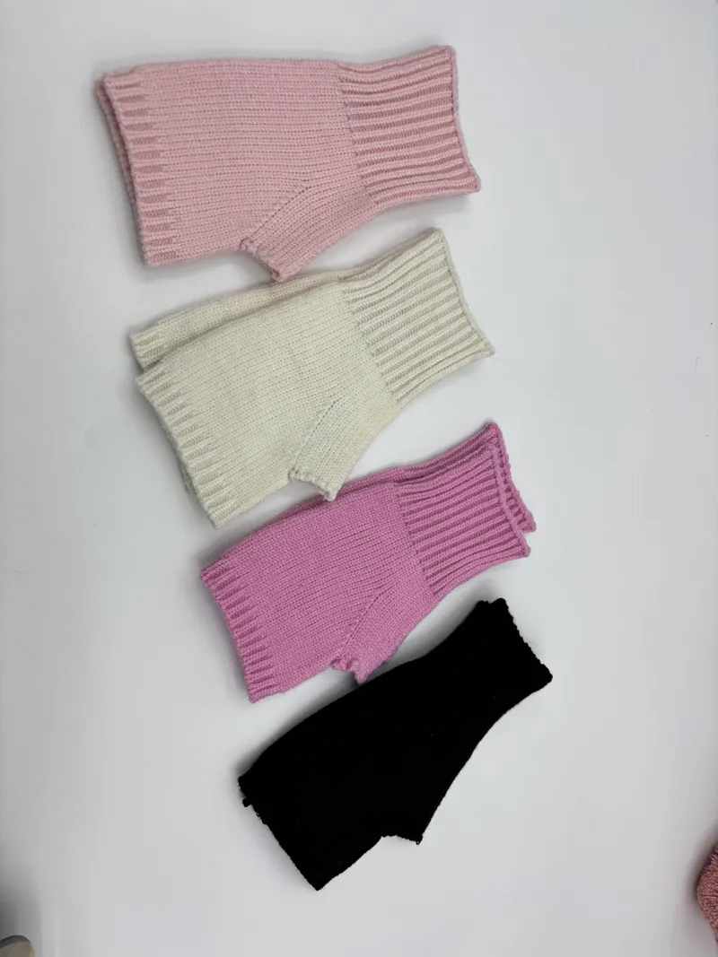 Vier fingerfreie Rippenstrickhandschuhe in Rosa, Creme, Flieder und Schwarz nebeneinander auf hellem Untergrund