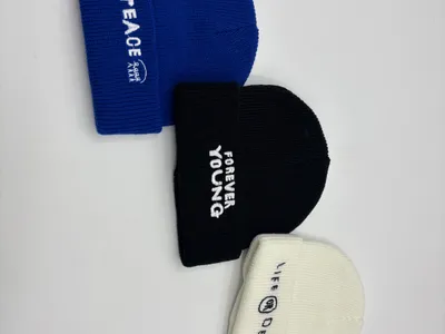 Drei gerippte Umschlagmützen in Blau, Schwarz und Creme mit bestickten englischsprachigen Slogans Peace, Forever Young und Life or Death