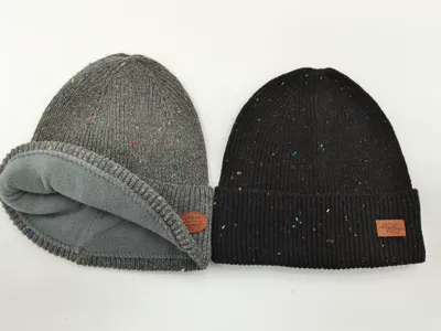 Zwei melierte Strickmützen nebeneinander: graue fleecegefütterte Rollmütze und schwarze Rippenmütze mit Umschlag und Leder-Patch