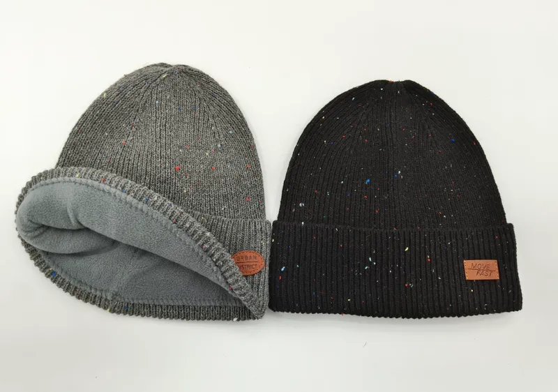Zwei melierte Strickmützen nebeneinander: graue fleecegefütterte Rollmütze und schwarze Rippenmütze mit Umschlag und Leder-Patch