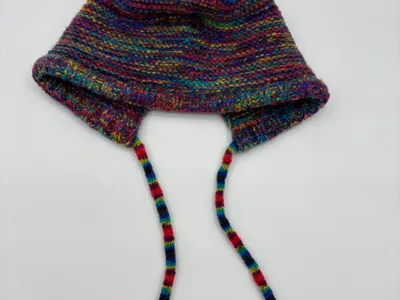 Handgestrickte Babyhäubchen aus mehrfarbigem Buntgarn mit Ohrenschutz und geflochtenen Bindebändern, Flachlage auf weißem Grund
