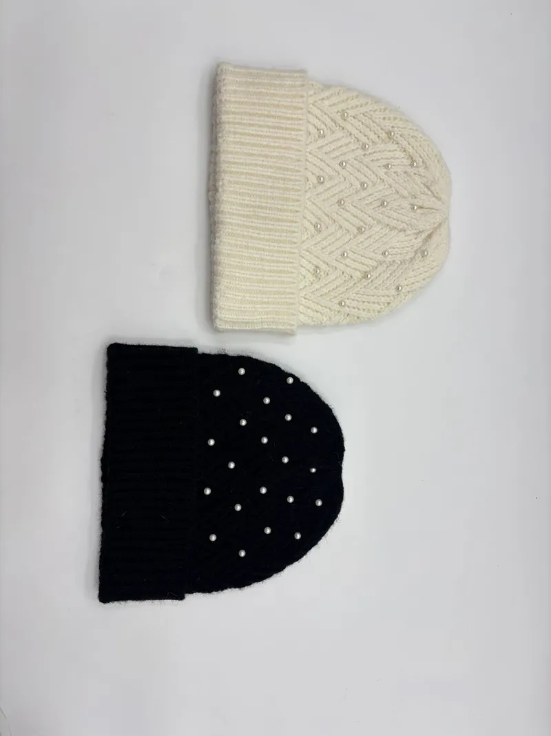 Zwei Rippenstrickmützen nebeneinander – eine in Creme mit Chevronmuster und eine in einfarbigem Schwarz, beide mit Perlenmotiven und Umschlagbündchen