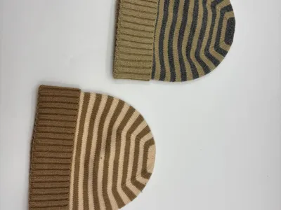 Zwei gestreifte Strickmützen mit Rippenbündchen in den Farbvarianten Khaki-Grau und Camel-Creme auf weißem Untergrund