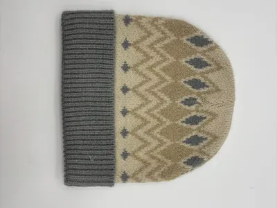 Beigefarbene Strickmütze mit grauem Fair-Isle-Rauten- und Zickzackmuster sowie grauem Rippenbündchen, Flachlage auf weißem Hintergrund