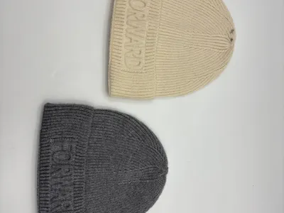 Zwei Rippenstrickmützen in Creme und Grau mit ton-in-ton geprägtem Forward-Logo am Umschlagbündchen, flach auf weißem Untergrund