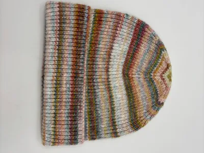 Gestrickte Wintermütze mit mehrfarbigen Space-Dye-Streifen in Rosa, Grün, Blau und Braun, gefaltetem Bündchen, auf weißem Hintergrund