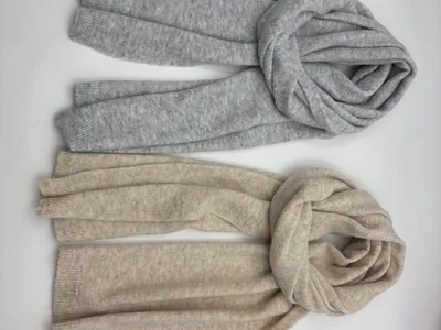 Zwei weiche Strickschals flach übereinandergelegt – einer in Hellgrau, einer in Beige, mit gerippten Enden und kuscheligen Strickdetails