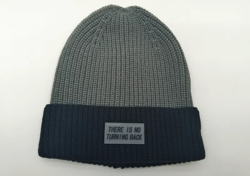 Zweifarbige Wintermütze in Grau und Schwarz mit grobem Rippenmuster und Gummi-Labelaufnäher mit Schriftzug auf dem dunklen Umschlag