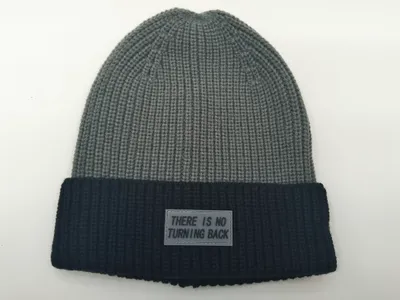 Zweifarbige Wintermütze in Grau und Schwarz mit grobem Rippenmuster und Gummi-Labelaufnäher mit Schriftzug auf dem dunklen Umschlag