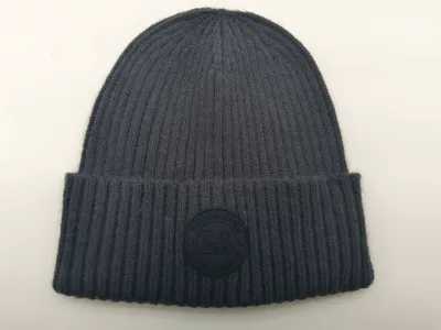 Anthrazitgraue Rippenstrick-Beanie mit gefaltetem Rand und rundem Gummi-Logoaufnäher mit der Aufschrift Change Is Possible, Flachaufnahme auf weißem Untergrund