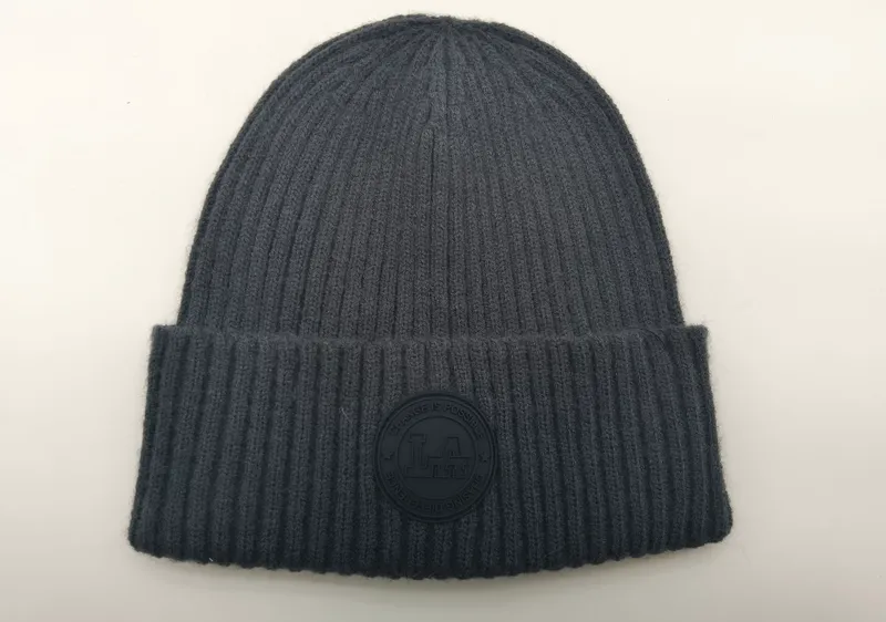 Anthrazitgraue Rippenstrick-Beanie mit gefaltetem Rand und rundem Gummi-Logoaufnäher mit der Aufschrift Change Is Possible, Flachaufnahme auf weißem Untergrund