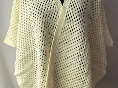 Cremefarbener Kimono-Cardigan mit Netzstrickmuster auf schwarzer Schneiderpuppe, mit luftigem Gittermuster und offenem Vorderteil