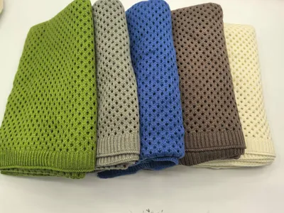 Fünf gestapelte offenmaschige Strickdecken aus Baumwolle in Grün, Grau, Blau, Braun und Creme auf weißem Untergrund